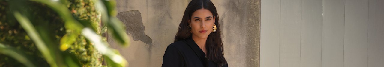 Woman in black top, standing in front of a light wall.