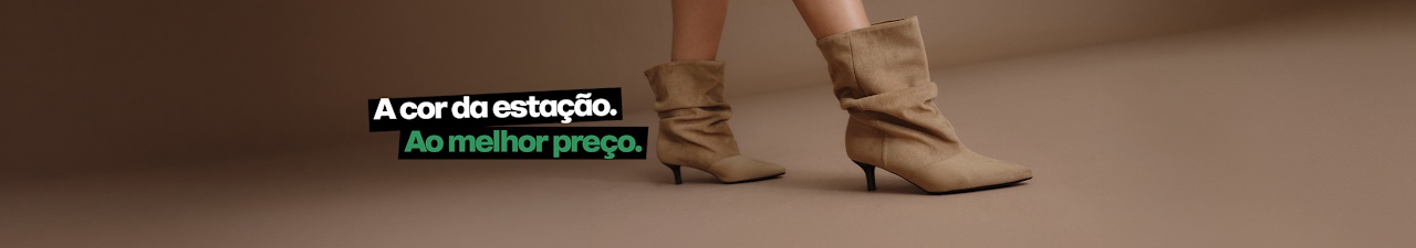 A close-up studio image shows a pair of beige slouchy ankle boots being worn against a neutral beige background. The boots feature a soft suede-like texture, pointed toes, gathered shafts, and slim kitten heels. Promotional text in Portuguese appears beside the footwear, including the price “34.99”.
