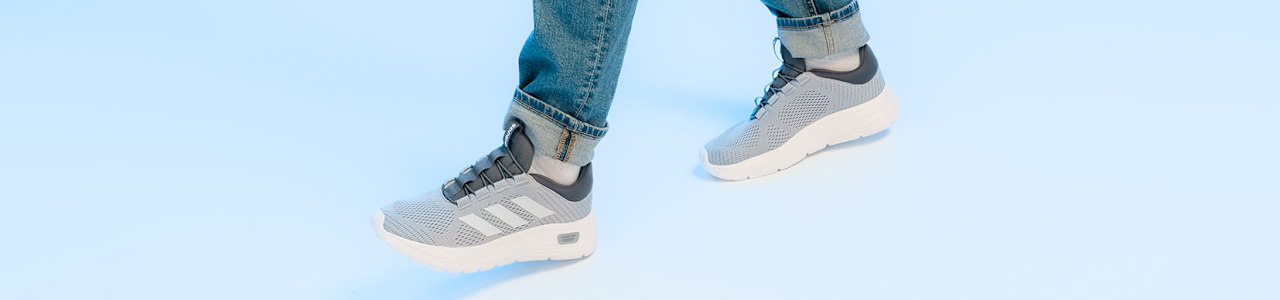 Close-up of a person in blue jeans, wearing grey Adidas sneakers with dark grey stripes.