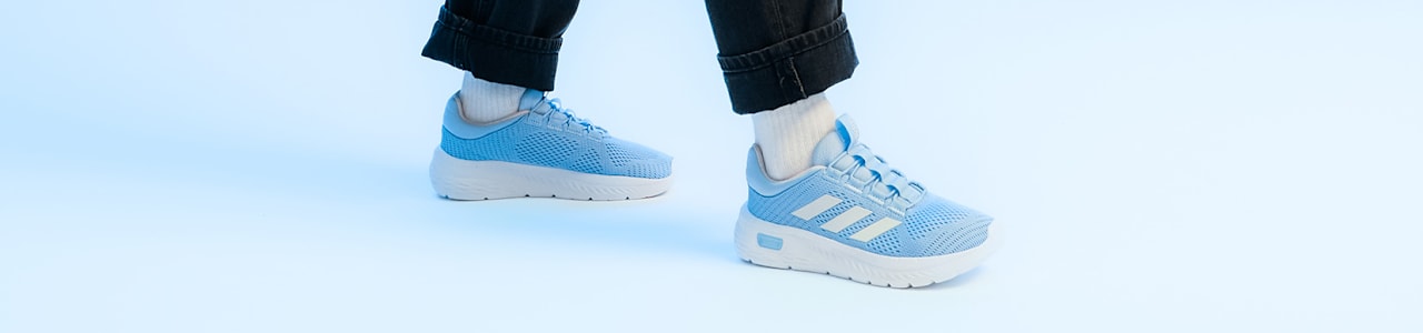 Close-up of a person wearing black jeans and light blue Adidas sneakers with white stripes.