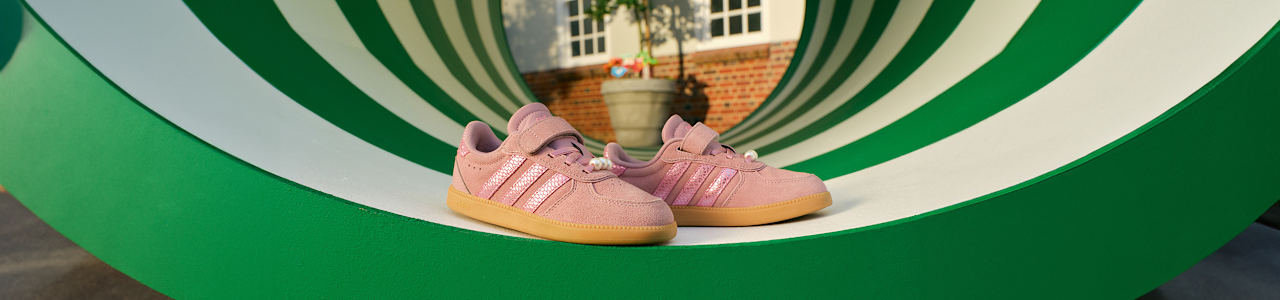 Pink Adidas sneakers displayed on a green playground tunnel.