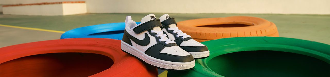 Black-and-white Nike sneakers displayed on colorful playground tires.
