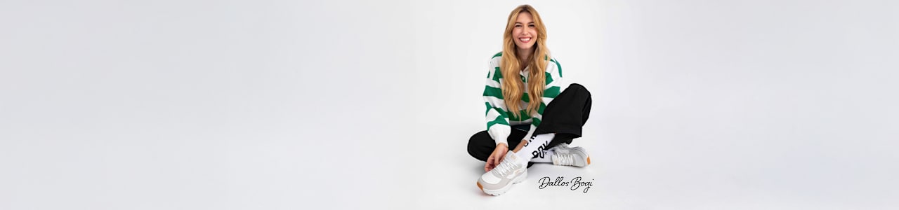 A woman sits on the floor wearing white sneakers with grey details.