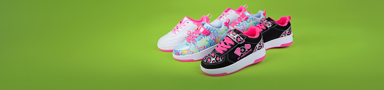 The image shows three colorful sneakers placed on a bright green background. The shoes have vibrant designs with pink accents, floral patterns, and multicolor details. They are arranged side by side, slightly angled to display the sides and tops.