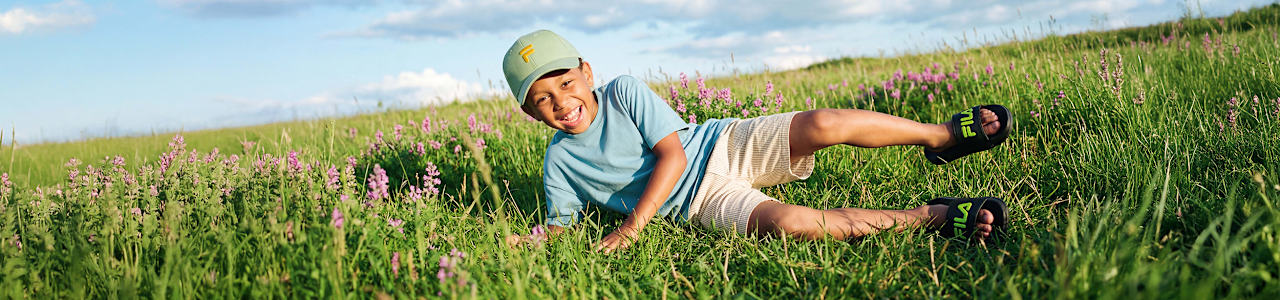 Wide banner of a child relaxing in a field wearing slide sandals.