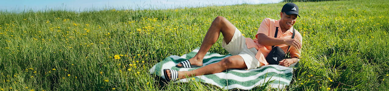 Close-up of striped slide sandals worn while lounging on a blanket in grass.