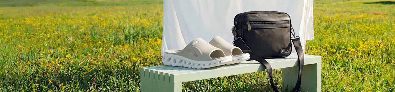 Beige slide sandals placed on a bench with a bag in a field setting.