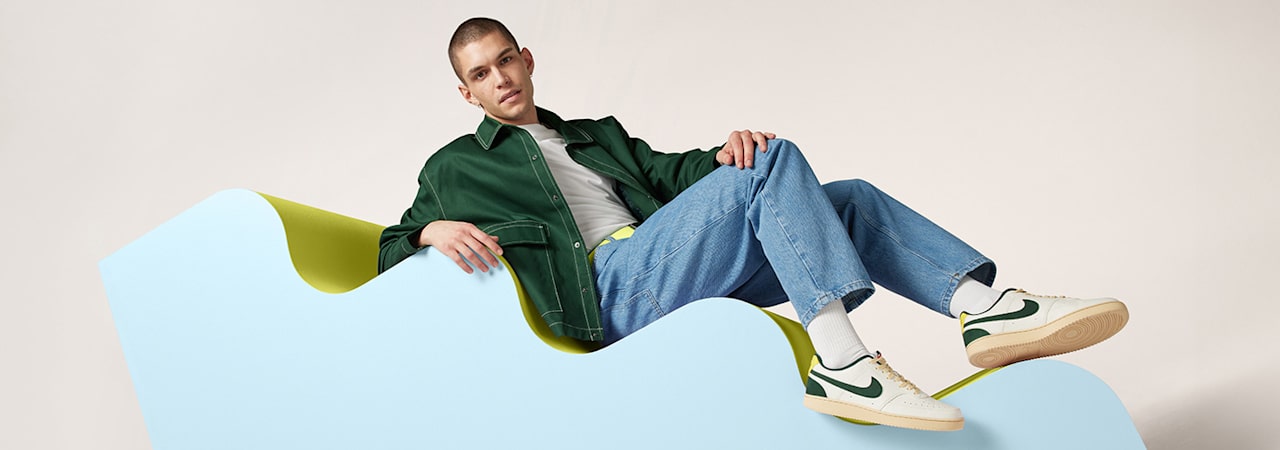 Man sitting on a light blue wavy structure with white Nike sneakers with a green logo