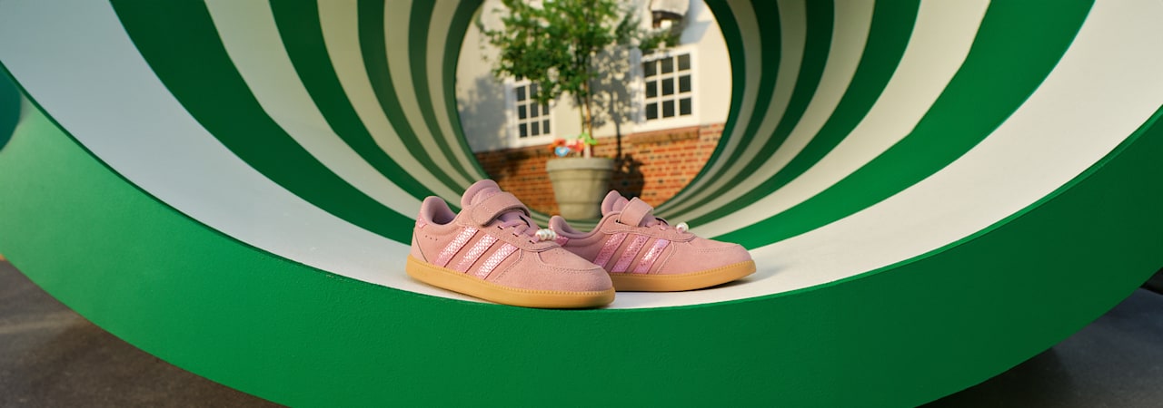 Pink Adidas sneakers displayed on a green playground tunnel.