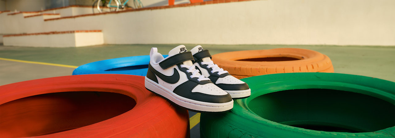 Black-and-white Nike sneakers displayed on colorful playground tires.