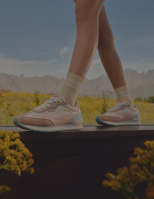 A close-up of legs standing in a field, wearing pastel pink and blue sneakers.