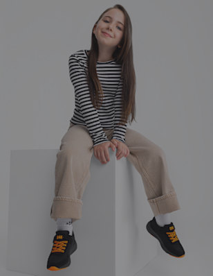 A girl sits on a block wearing black sneakers with orange details.