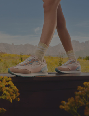 A close-up of legs standing in a field, wearing pastel pink and blue sneakers.