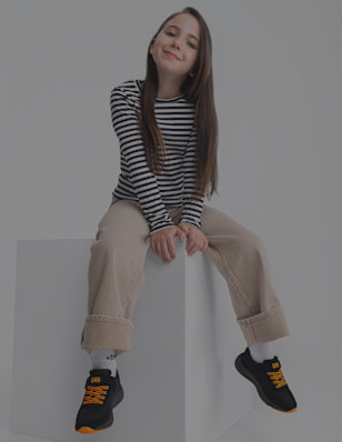 A girl sits on a block wearing black sneakers with orange details.