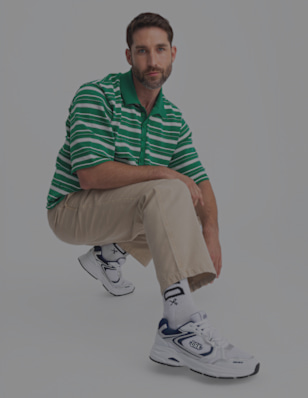 A man crouches in beige pants and striped socks, wearing white sneakers with blue details.