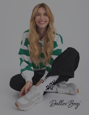 A woman sits cross-legged, wearing black pants and white sneakers with grey details, next to a logo that reads "Dallos Bogi".