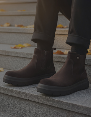 Close-up of brown Esprit Chelsea boots on stone steps with yellow autumn leaves around.