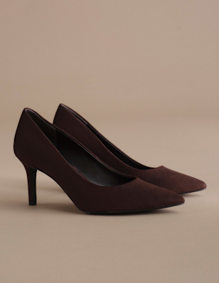 A pair of dark brown pointed-toe pumps is displayed on a neutral beige background. The shoes feature slim high heels and a smooth finish, creating a sleek and elegant silhouette in a clean studio setting.
