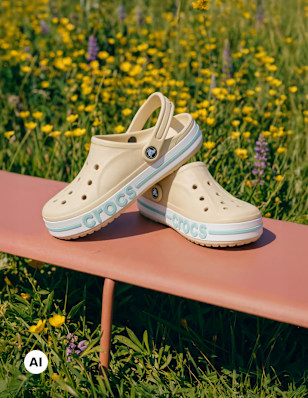 Pair of beige Crocs-style clogs placed on a bench outdoors in a sunny field.