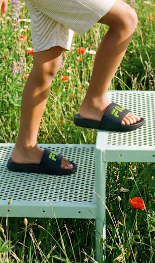 Close-up of black slide sandals worn while stepping onto a metal platform outdoors.