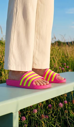 Close-up of pink slide sandals with neon stripes worn while standing on a bench outdoors.