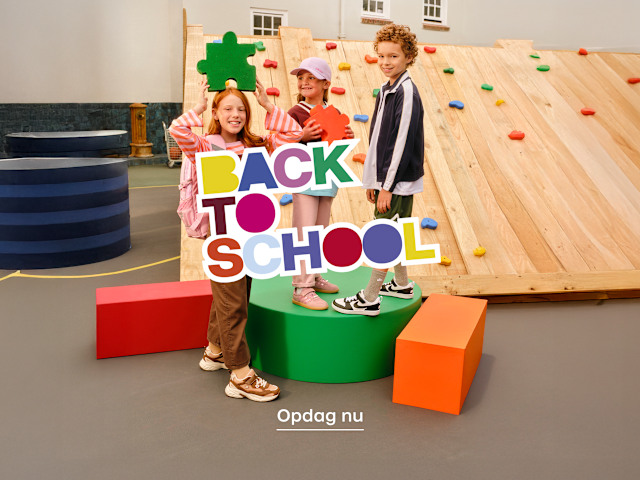Children posing with a colorful “Back to School” sign in front of a climbing wall.