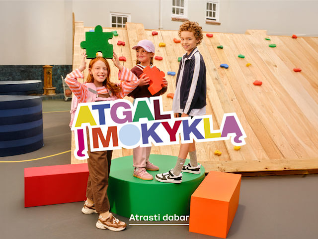 Children posing with a colorful “Atgal į mokyklą” (Back to School) sign.