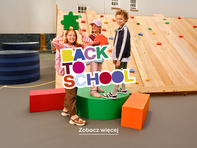 Children posing with a colorful “Back to School” sign in front of a climbing wall.