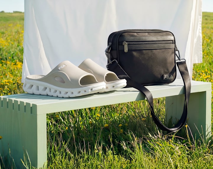 Beige slide sandals placed on a bench next to a bag in a field.