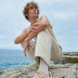 Young male squatting on rocks in front of ocean