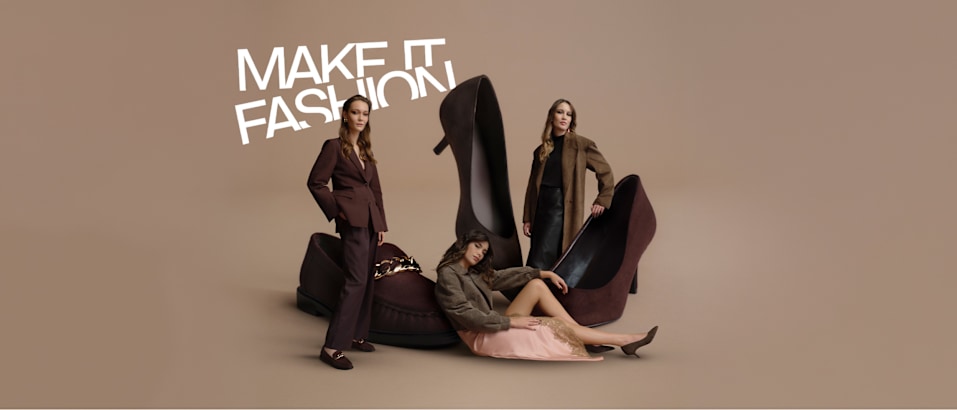 Fashion campaign image on a beige background featuring oversized dark brown loafers and high heels. Three models are posed around the shoes, wearing coordinated outfits in brown and neutral tones. The slogan “MAKE IT FASHION” appears in large white lettering in the upper left corner, highlighting a seasonal fashion footwear collection in chocolate brown shades.