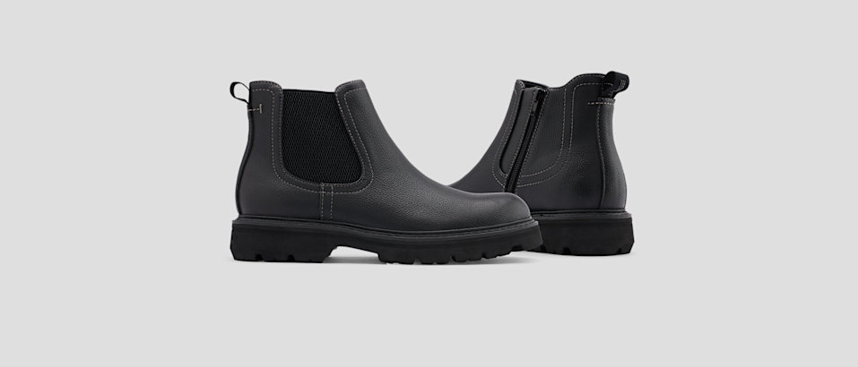Pair of black Chelsea boots with elastic side panels and rugged soles on a light gray background.