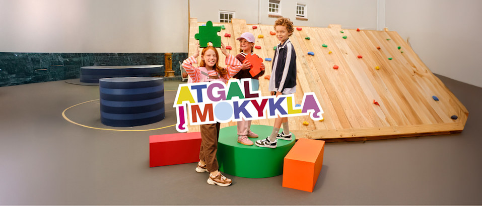 Children posing with an “Atgal į mokyklą” (Back to School) sign.