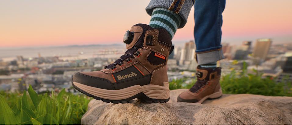 Explore Outdoor image showing brown hiking boots on a scenic rocky viewpoint.