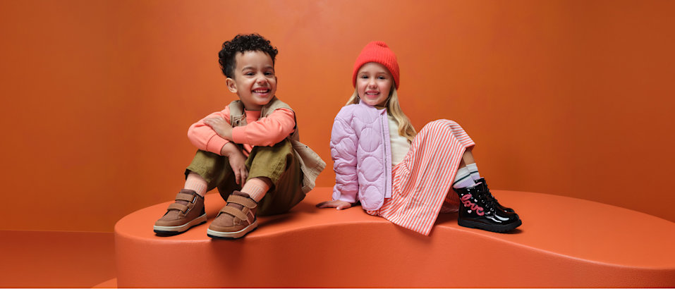 two kids with boots sitting on a podest with orange background