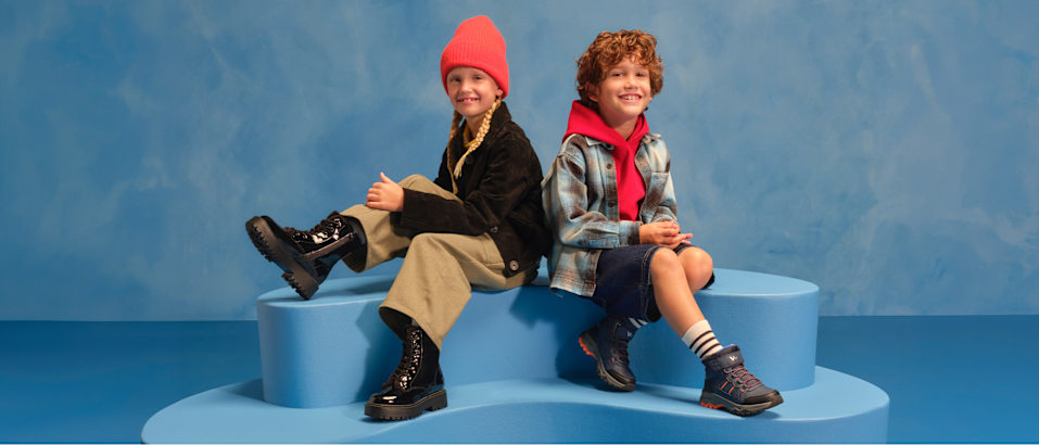 two kids with boots sitting on a podest with blue background