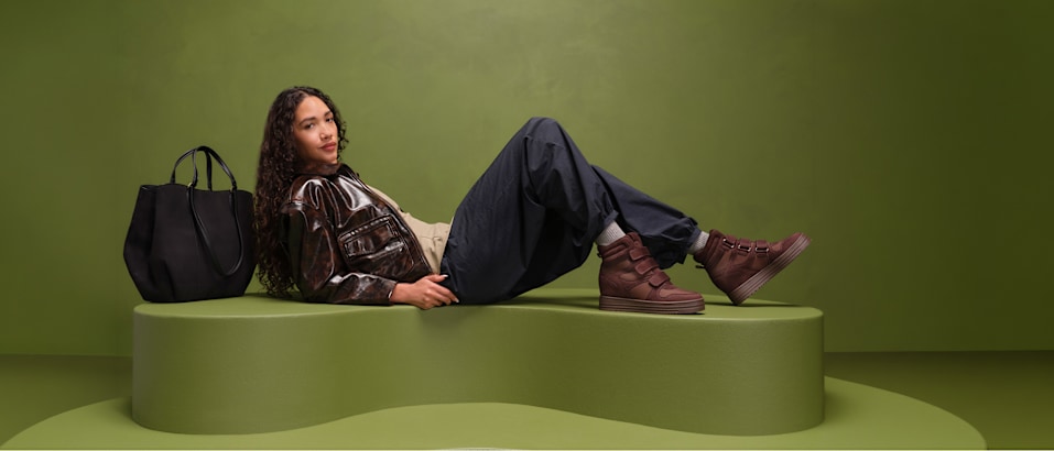 women with wedge sneaker sitting on a pedestal with green background